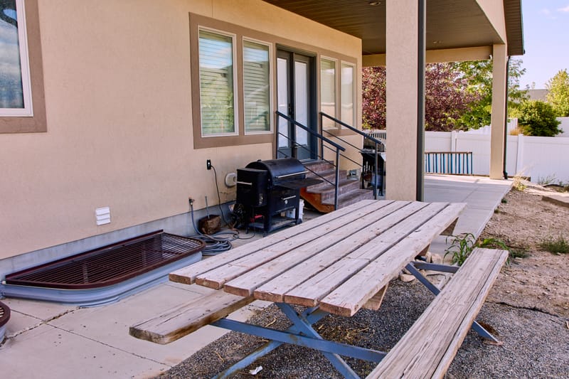 The covered patio, with a smoker, a gas grill, and a long picnic table under the roofline.