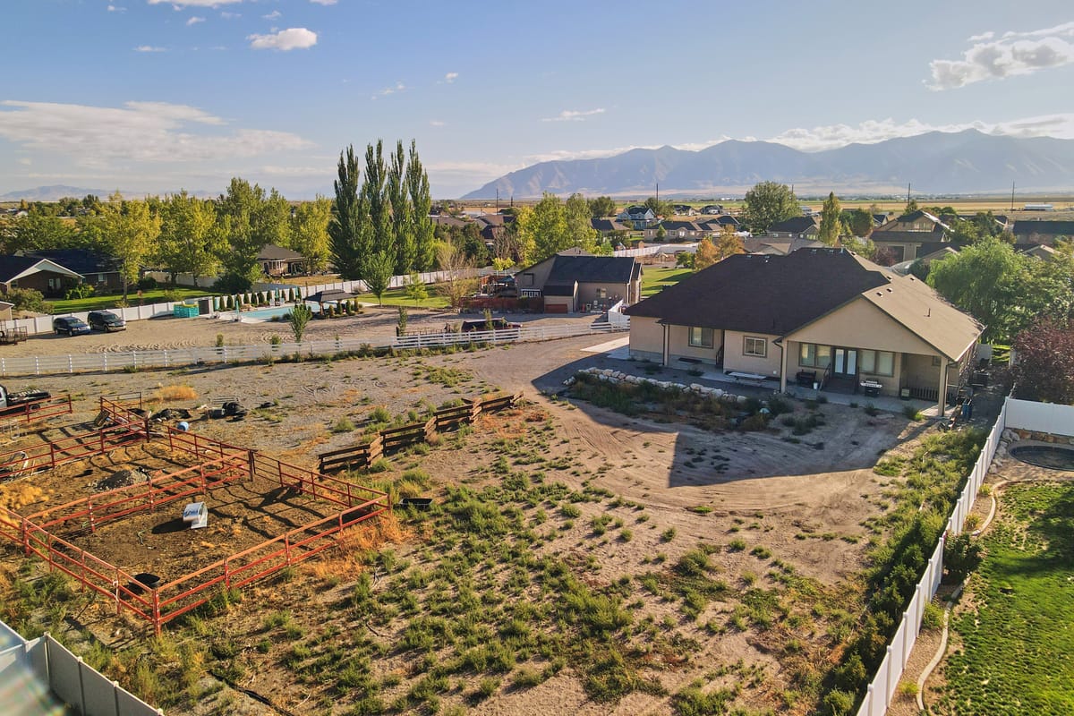 Aerial view of Desert Peak Lodge on open ground in the Tooele Valley, with three fenced corrals in the foreground and mountain ranges behind.