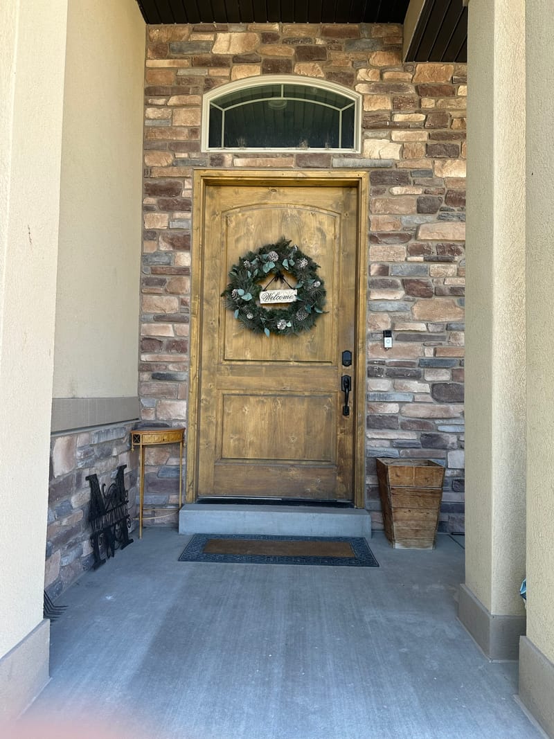 The front entrance — a stained wood door with a wreath, set in stone, with a keypad lock mounted beside the handle.