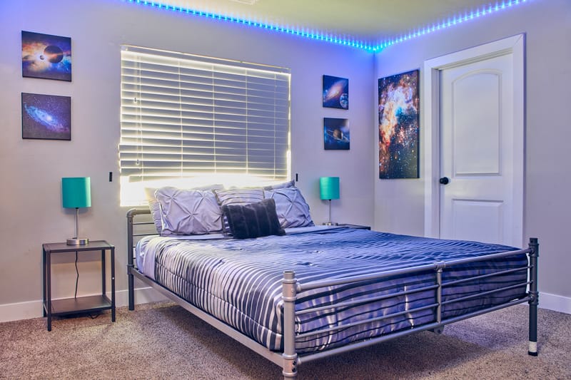 The Galaxy Room, with a queen bed, framed galaxy prints, and an LED light strip running along the ceiling line.
