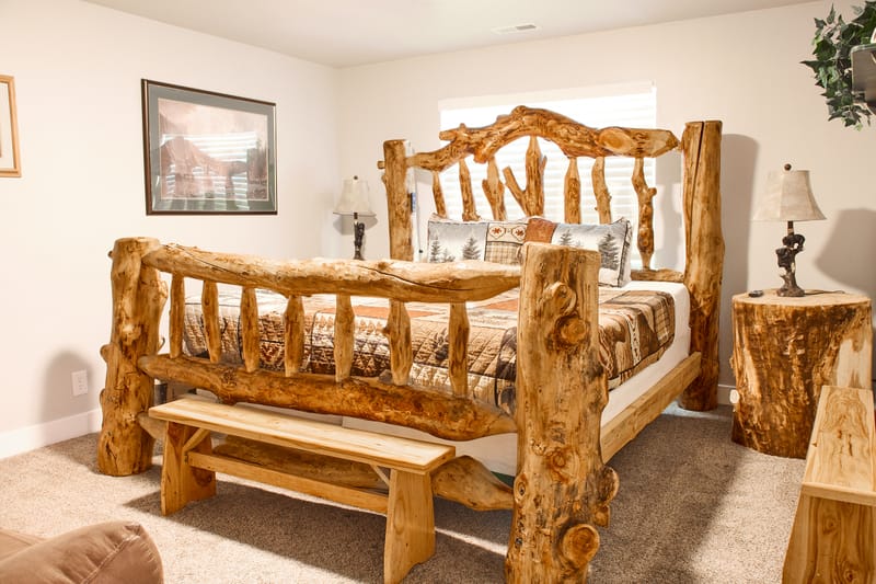 The Log Cabin Room, with a hand-carved log king bed, matching log side tables, and a bench at the foot of the bed.