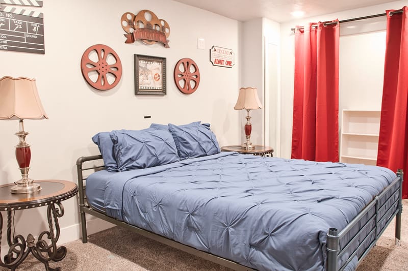 The Theater Room, with a queen bed, framed film reels and cinema prints on the wall, and floor-length red curtains.
